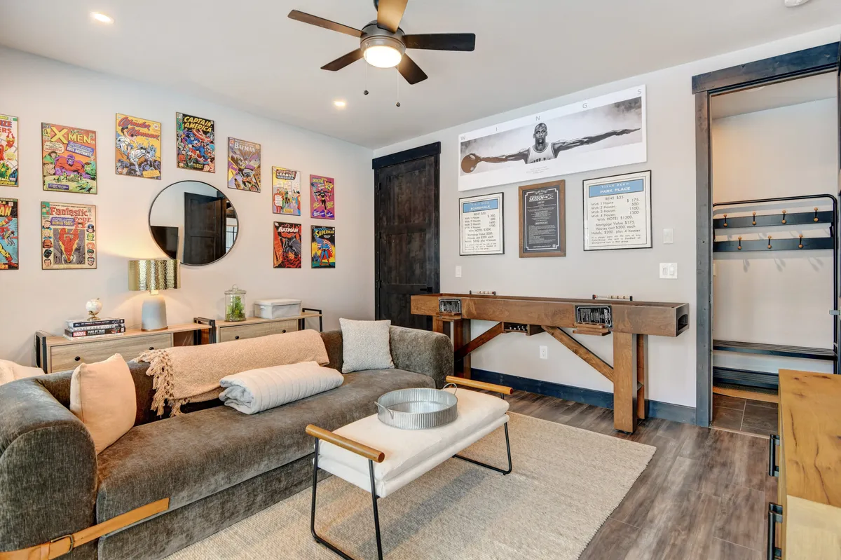A vibrant interior living space featuring comic book wall art, a round mirror, a plush sofa, a coffee table, and a wooden console table. The playful decor and cozy seating make it ideal for relaxed gatherings, game nights, or enjoying a movie marathon.