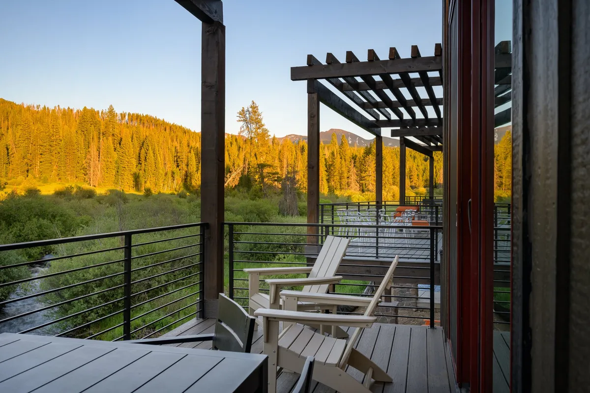 A wooden deck bordered by lush greenery, with outdoor chairs and a pergola overlooking sweeping mountain views. The setting invites guests to savor nature, socialize, and enjoy stargazing or sunset moments.