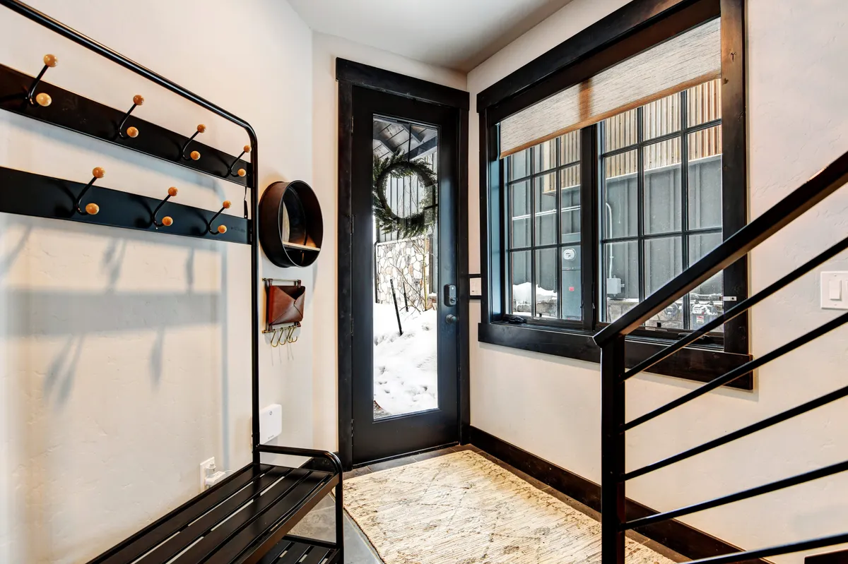 A welcoming entryway featuring a black coat rack, entry bench, a door adorned with a wreath, and a large window letting in abundant natural light. The scene exudes warmth and hints at the transition between outdoor adventures and the cozy interior.