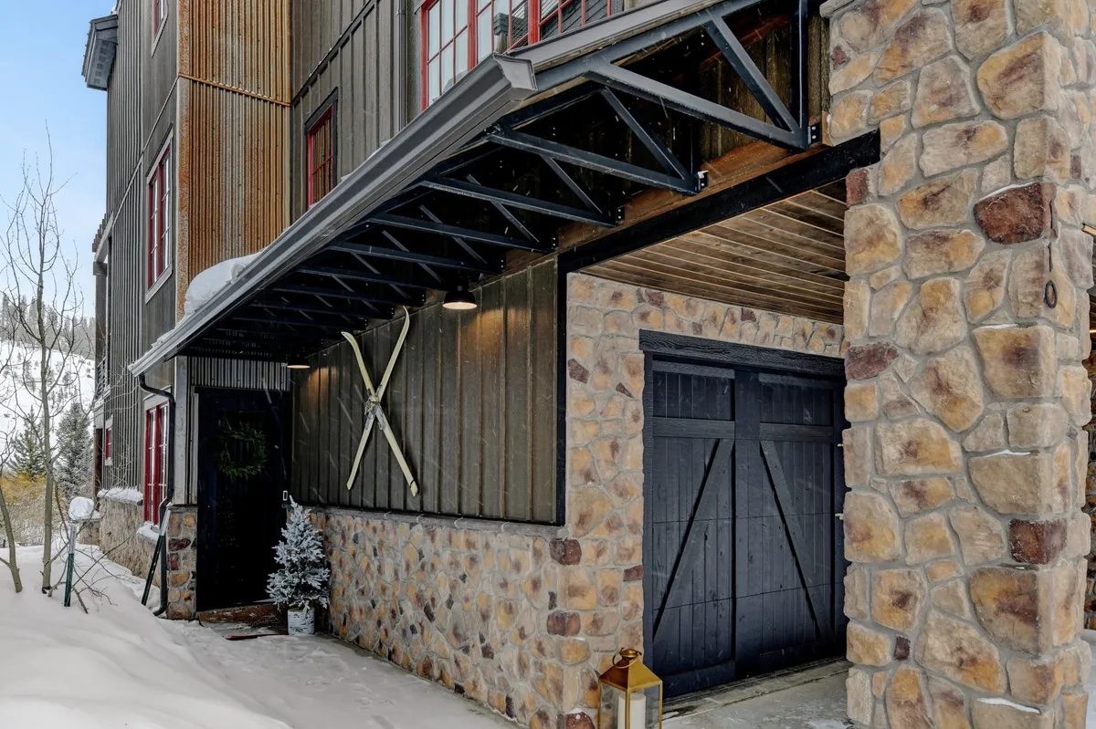 The exterior showcases a welcoming stone wall, wooden beams, and decorative ski poles, set against a snowy landscape. The scene evokes arrival, seasonal activities, and family gatherings, making it highly relatable for groups arriving for a shared experience.