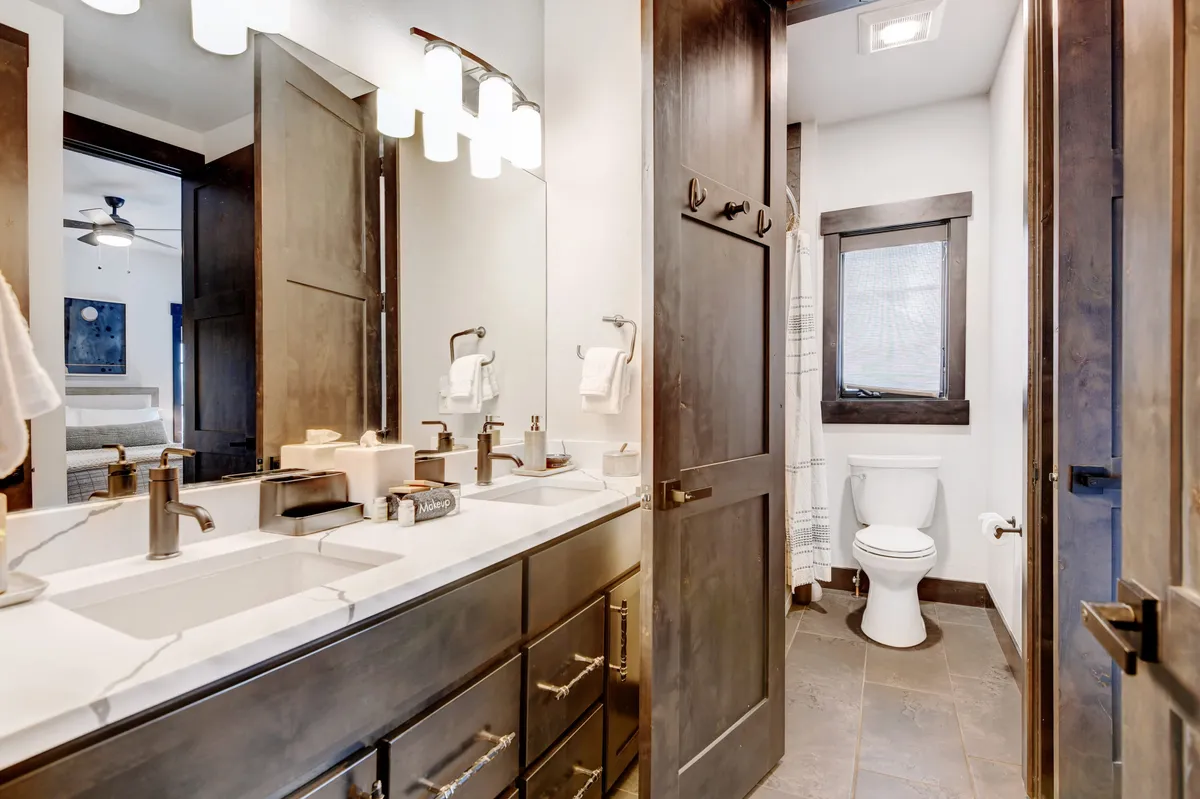 A stylish bathroom with a double sink vanity, modern light fixtures, dark wood cabinetry, and a toilet. The space feels fresh and inviting, with ample lighting and a clean, organized look.