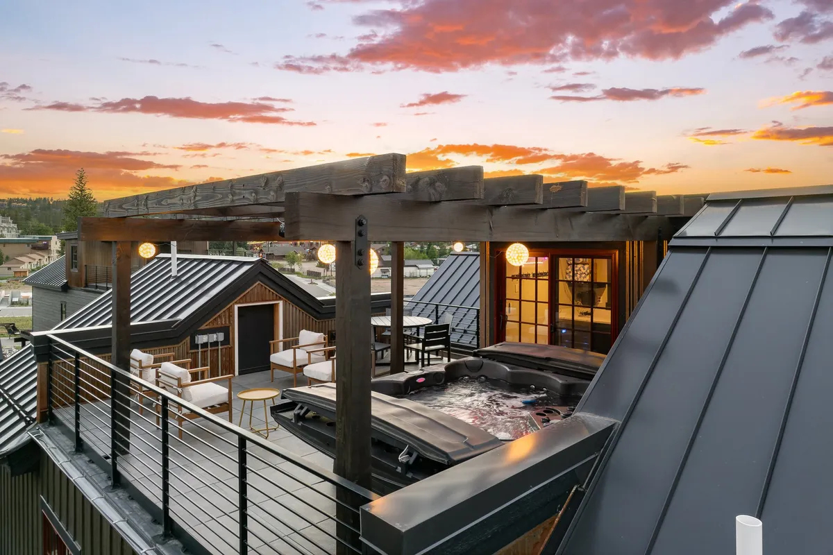 A picturesque exterior scene of the rooftop patio showcasing a bubbling hot tub, comfortable seating, and a stunning sunset sky. The layout encourages group gatherings and tranquil solitude alike.