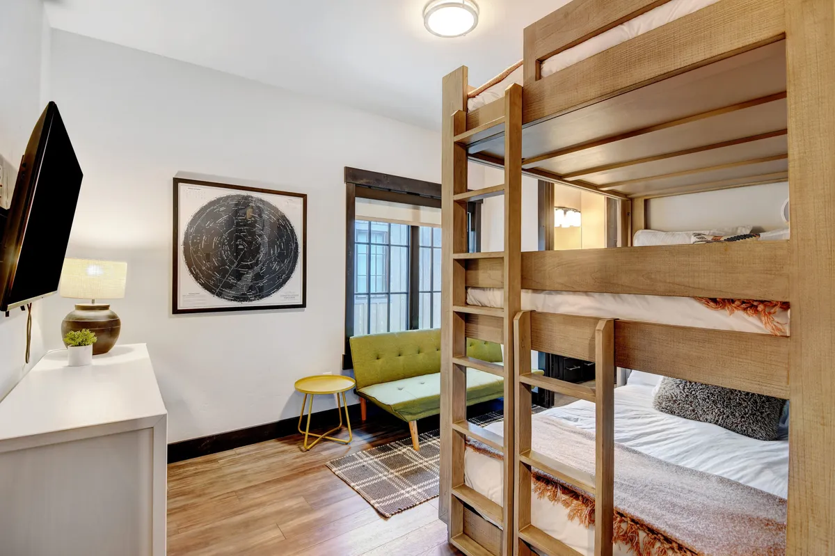 A playful bunk room with multiple bunk beds, a green sofa, colorful wall art, and a television. The space is designed for comfort and fun, ideal for families or younger guests to relax and bond.