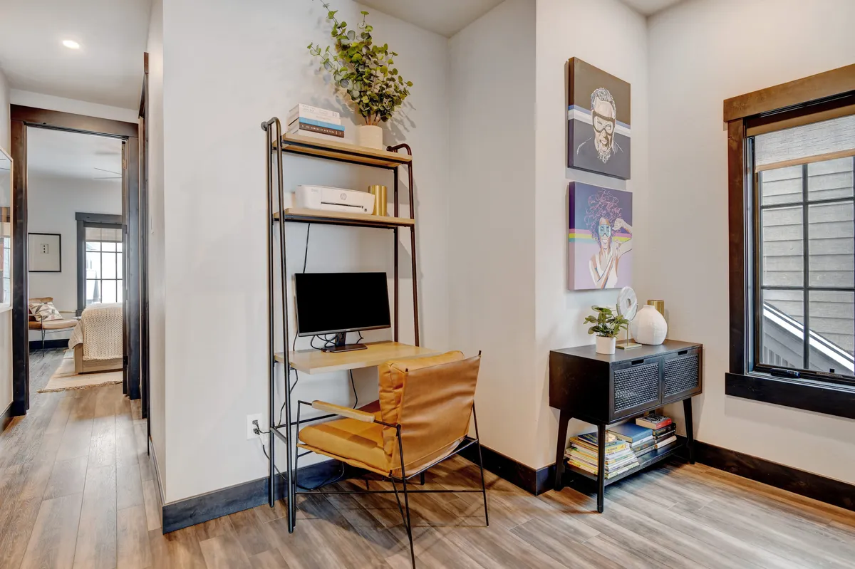 A thoughtfully designed work desk area featuring a computer, inspirational wall art, a plant on a shelf, and an inviting chair. The setup fosters productivity and creativity, making it ideal for remote work or study during a stay.
